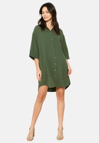 Green short-sleeve dress made of lightweight fabric, featuring a button-down front, oversized fit, and a curved hem.