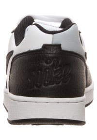 Czarne skórzane trampki z białymi akcentami, z teksturowanym tyłem, wyraźnym logo "nike" i białą gumową podeszwą.