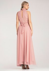 Tylny widok różowej sukienki maxi z dekoltem na halter, otwarciem w kształcie łezki, przymocowanym paskiem, teksturowanym materiałem oraz warstwową, zwiewną spódnicą.