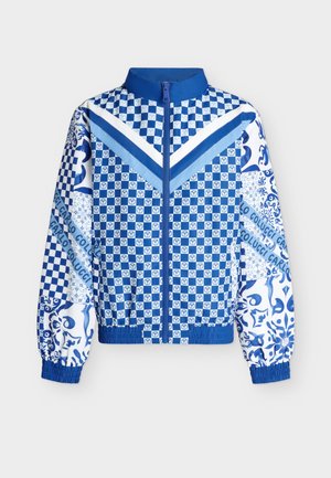 Veste à carreaux bleue et blanche avec fermeture éclair, rayures en chevron sur la poitrine, poignets élastiques et motifs floraux et logo mélangés sur les manches.