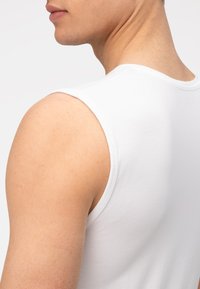 Witte katoenen tanktop met een ronde halslijn en ruime armsgaten, die een soepele textuur en een aansluitend ontwerp benadrukt.