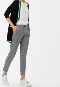 Grå rutiga byxor med slim fit, med sidfickor och rak front, ihop med en svart cardigan med grön kant.