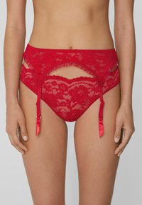Rote Spitzenunterwäsche mit Rüschen, Aussparungen und Satinakzenten. Mit verstellbaren Trägern für eine optimale Passform. Weicher, transparenter Stoff.