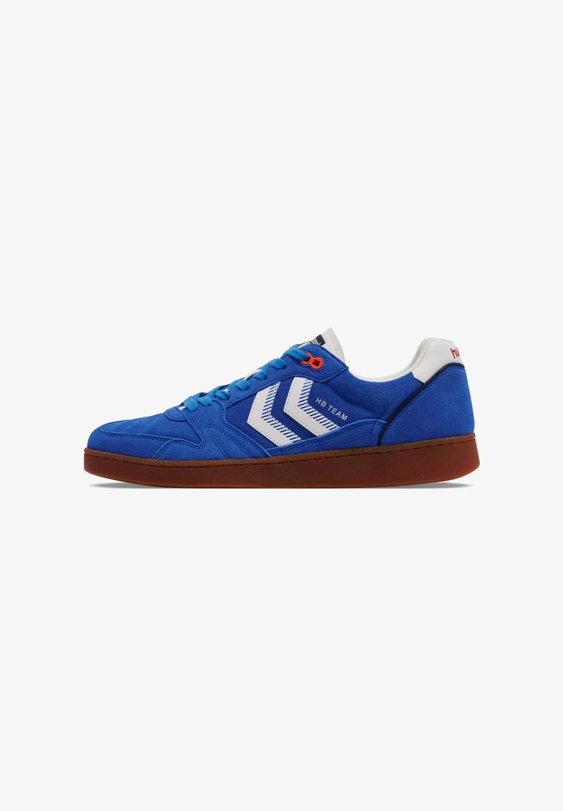 Baskets en suede bleu avec des accents rouges et des rayures blanches diagonales. Présentent une semelle en caoutchouc et un système de laçage. Nom de la marque au niveau du talon.