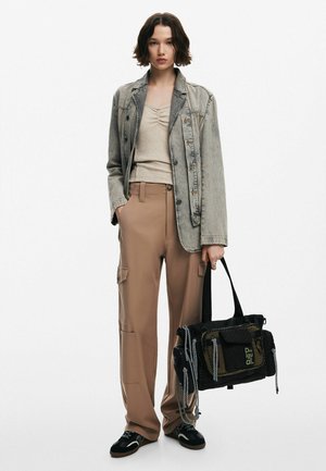 Graue Jeansjacke, beiger figurbetonter Oberteil, hellbraune Cargo-Hosen, schwarze und grüne Tasche mit Akzenten und schwarze Sneakers mit weißen Details.