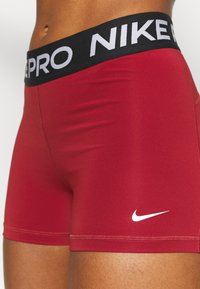 Pantalones cortos deportivos rojos de tela elástica que presentan una cinturilla negra con "NIKE PRO" en blanco y un pequeño logo de Swoosh de Nike en blanco.