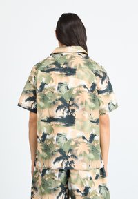 Korte mouw shirt in licht perzik met groen en zwart palmboomprint; relaxte pasvorm met een puntige kraag en een gladde textuur.