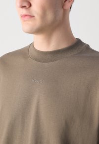 T-shirt vert olive en coton doux, avec un col rond et un petit logo "HUGO" ton sur ton sur la poitrine.