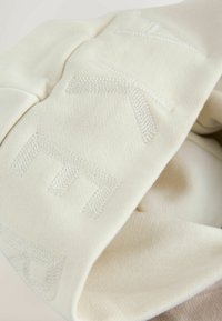 Kremowa bluza z teksturowanej tkaniny, z subtelnym wytłaczanym wzorem. Projekt obejmuje złożone mankiety i gładkie wnętrze.