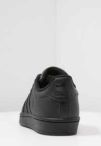 Baskets en cuir noir avec surface texturée, trois bandes lat érales, col rembourré et semelle en caoutchouc. Logo embossé sur le talon.