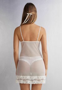 Witte doorschijnende lingerie set met dunne verstelbare bandjes. Bevat een kanten zoom en een string snit, die een delicaat bloemmotief benadrukt.