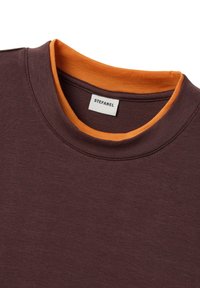 Nahaufnahme eines braunen Sweatshirts mit Rundhalsausschnitt, einem orangefarbenen Innenkragen und einem weißen Etikett mit der Aufschrift "STEFANEL".