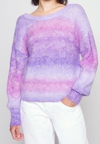 Stickad tröja i gradientnyanser av lila och rosa, med vid halsringning och ribbade muddar. Mjuk textur och lös passform. Matchad med vita byxor.