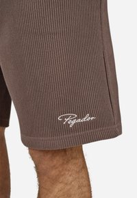 Shorts marron côtelés en tissu texturé, avec un logo "Pegador" blanc sur l'ourlet.
