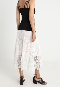 Svart åtsittande linne med tunna axelband, tillsammans med en vit spetsmidikjol med blommönster. Svarta klackskor med blockklack.