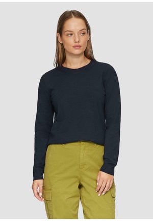 Navyblauwe crewnecktrui van een textuurstof, met lange mouwen. Gecombineerd met olijfgroene cargobroek, wat de casual stijl benadrukt.