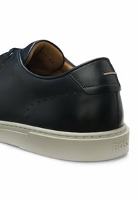 Baskets en cuir noir avec semelle blanche, coutures visibles, doublure intérieure beige et nom de la marque embossé sur le talon.