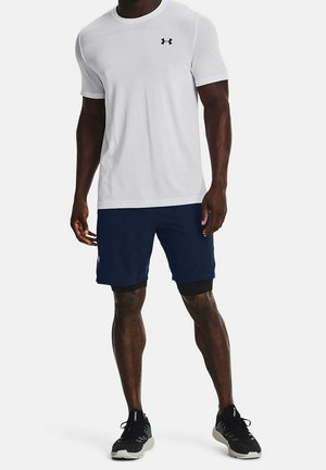 Hvid kortærmet træningsshirt med et sort logo, kombineret med navy shorts med sorte kanter og sorte løbesko med grå såler.