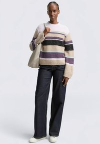 Gebreide trui met horizontale strepen in beige, paars, zwart en teal. Gecombineerd met donkerblauwe jeans met wijde pijpen en crèmekleurige sneakers.
