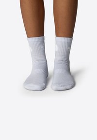 Calcetines de crew blancos con textura acanalada, que presentan un logo en el lateral, destacando el material elástico y un ajuste ceñido alrededor de los tobillos.