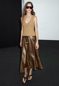 Hnědý pletený top s výstřihem do V a květinovými detaily, v kombinaci s hnědou koženou midi sukni a hnědými žabkami. Modelka nosí oversized sluneční brýle.