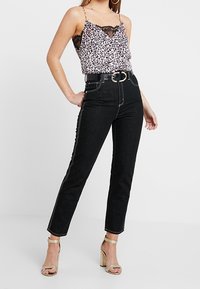 Sort høj talje jeans med en slim fit, kontrasterende hvid syning, parret med en leopardmønstret camisole med blonder.