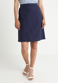 Navy blue knee-length skirt with floral eyelet pattern, smooth texture, and a fitted waistband. Matched with a striped top and white heels.