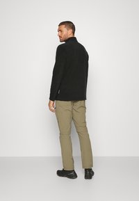 Fleecejacke in Schwarz mit hohem Kragen. Kombiniert mit hellen khakifarbenen Cargo-Hosen und schwarzen Wanderschuhen. Minimalistisches Design.