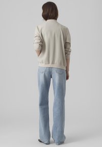 Light beige bomber jacket with ribbed cuffs and hem, paired with light blue wide-leg jeans, viewed from the back. Smooth texture, casual fit.