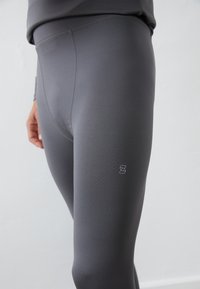 Pilki, aukštai talpūs leggingai, pasižymintys lygiu, elastingu audiniu ir subtilia logotipo detale kairėje šlaunyje.