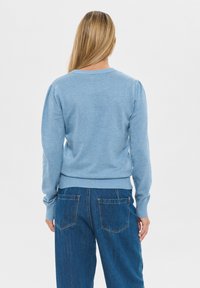 Svetlo modra pletena jopica z dolgimi rokavi in ribanim robom, z okroglim ovratnikom in subtilnim nabranim detajlom na rami. Nosi se z kavbojskimi hlačami.