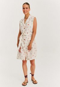 Sukienka bez rękawów z lnu na jasnym beżowym tle, w kwiatowe wzory w kolorach czerwonym i fioletowym, z wiązanym paskiem w talii.