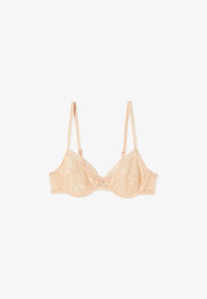 Reggiseno beige in pizzo con ferretto, spalline sottili regolabili e piccolo fiocco centrale, disteso su uno sfondo bianco.