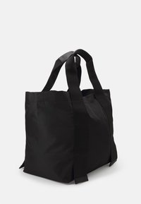 Stor svart weekendväska med breda tyghandtag, stående upprätt på en enkel vit bakgrund, svängd något åt höger.