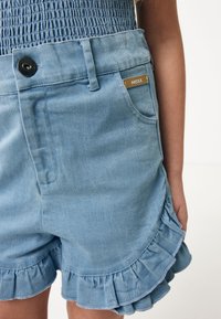 Ljusblå denimshorts med volangkant, med framknäppning, sidofickor och en liten guldfärgad logotag.