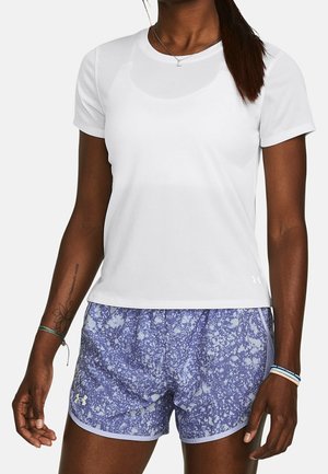 Vrouw draagt een effen wit T-shirt met korte mouwen en blauwe sportshorts met een patroon en een klein logo op het linkerbeen.