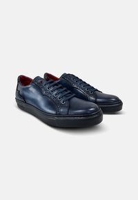 Zapatillas de cuero azul marino con detalles de brogue, puntera redondeada y interior rojo en contraste, con suela de goma texturizada negra y seis ojales.