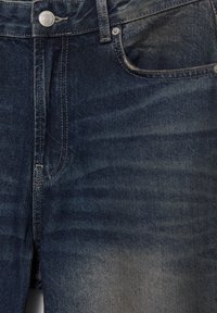 Dunkelblaue Jeans aus Denim mit klassischem Fünf-Taschen-Design, dezentem Verblassen und einem Metallknopfverschluss. Der Stoff hat eine glatte Textur.