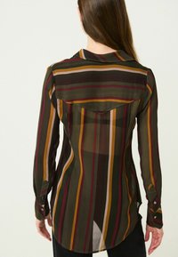 Chemise en chiffon présentant des rayures verticales en vert foncé, bordeaux et moutarde. Poignets à boutons et ourlet incurvé avec un empiècement au dos.