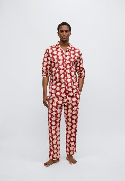 Set de pijamale roșii și crem, cu model, constând dintr-o cămașă cu nasturi și mâneci lungi și pantaloni asortați, ambele decorate cu motive stelare.