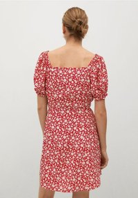 Rotes Blumenbekleid mit kurzen Puffärmeln, Quadrat-Ausschnitt und taillierter Taille. Mit einem weißen Blumenmuster auf dem Stoff.