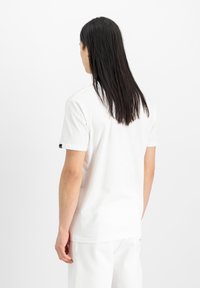 Tricou alb cu mânecă scurtă din material de bumbac, cu un decolteu rotund și un mic accent cu logo pe mânecă. Textură netedă.