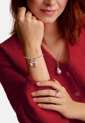 Silver bracelet with charms, including a pearl and decorative element; matching pearl pendant necklace; red knitted sweater; polished nails.