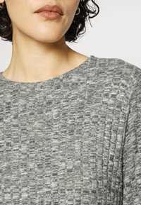 Maglione grigio a maglia con un motivo strutturato in diverse sfumature di grigio. Collo rotondo e tessuto morbido. Senza loghi o decorazioni visibili.