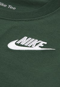 Zelena pamučna majica s istaknutim bijelim vezom Nike logom na prsima, s okruglim izrezom i kratkim rukavima.