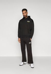 Zwarte set bestaande uit een sweatshirt en broek, voorzien van een capuchon, een voorvak en een logo in contrasterende kleuren. Gemaakt van zachte stof met een comfortabele, losse pasvorm.