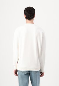 Hvit hettegenser med avslappet passform, droppede skuldre, ribbede mansjetter og nederkant; kombinert med lyseblå jeans. Glatt tekstur, minimal design.