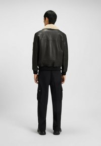 Czarna skórzana kurtka z kremowym kołnierzem z owczej wełny, prążkowanymi mankietami i paskiem, zestawiona z czarnymi spodniami cargo. Widoczne subtelne detale w szyciu.