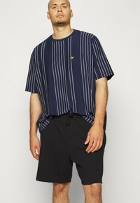 Camicetta a righe blu navy a maniche corte con colletto rotondo e tasca, caratterizzata da righe verticali bianche. Abbinata a pantaloni corti neri con coulisse.