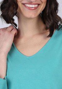 Türkiser V-Ausschnitt-Oberteil aus weichem, glattem Stoff. Hat ein einfaches Design mit lockerer Passform und langen Ärmeln.